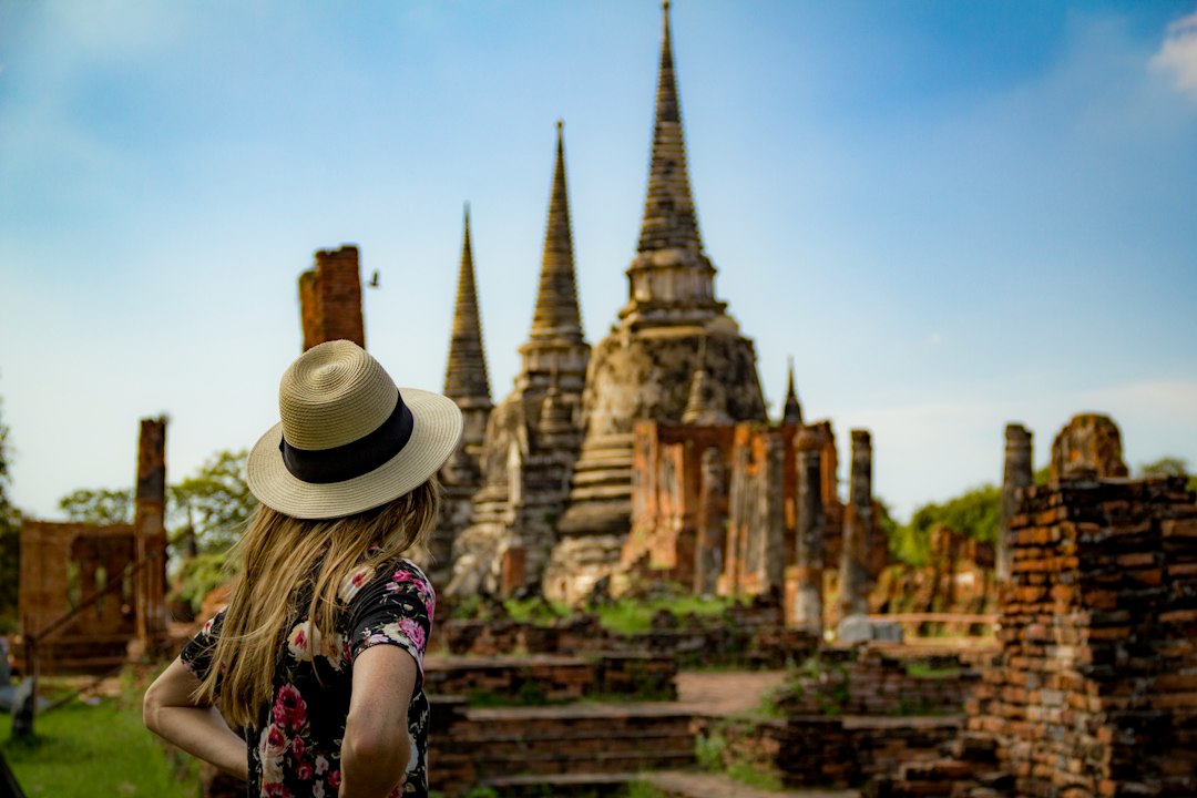 Ayutthaya: woman in pink and white floral shirt and brown hat standing near brown concrete building during**