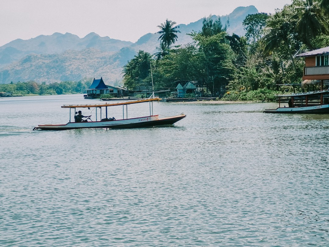 Kanchanaburi: a boat traveling down a river next to a lush green hillside**