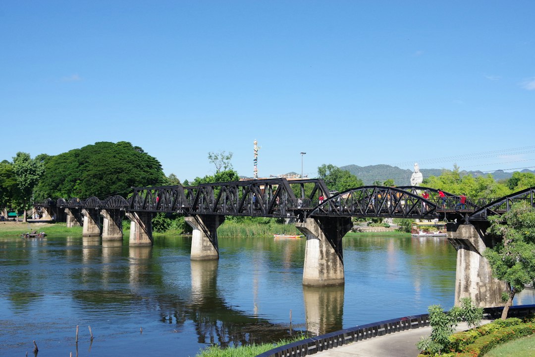 Kanchanaburi: gray concrete bridge over river under blue sky during daytime**