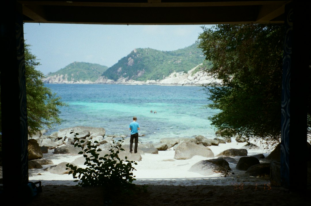 Koh Tao: Man on rocky beach overlooking clear blue ocean and mountains**