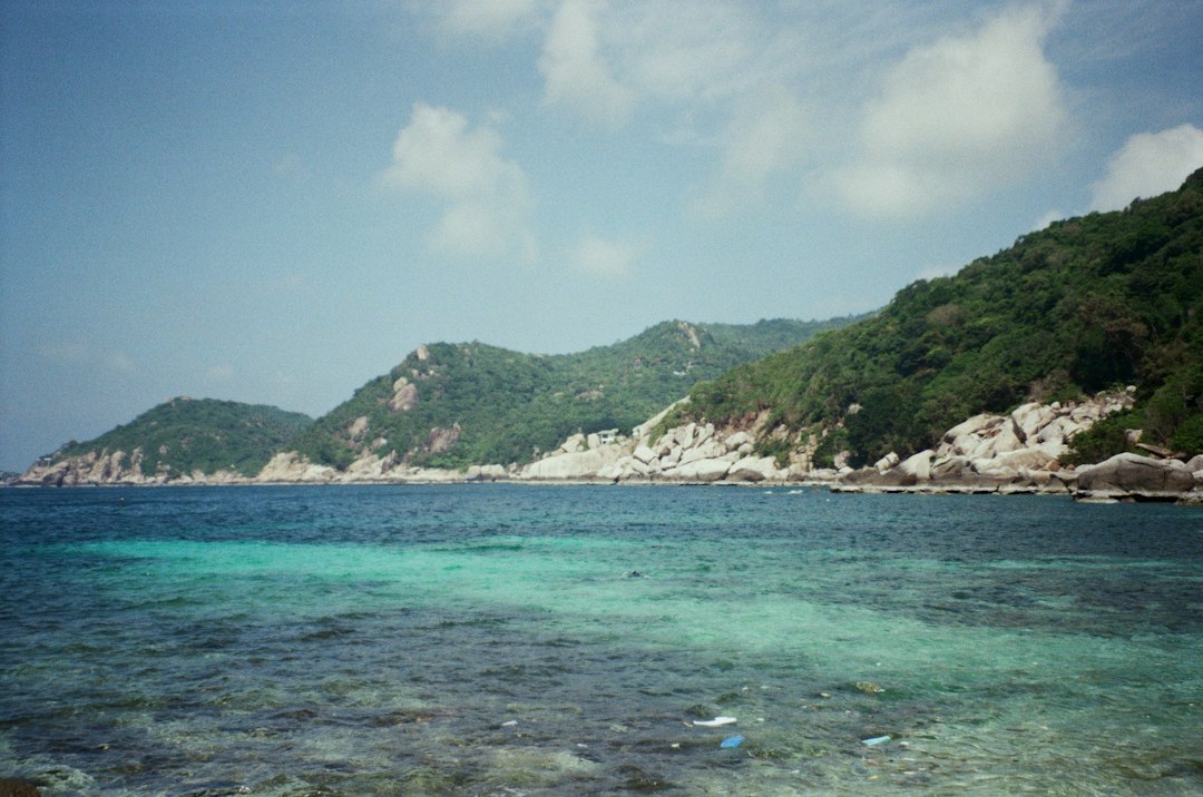 Koh Tao: Tropical blue ocean and green, rocky coastline under blue sky**